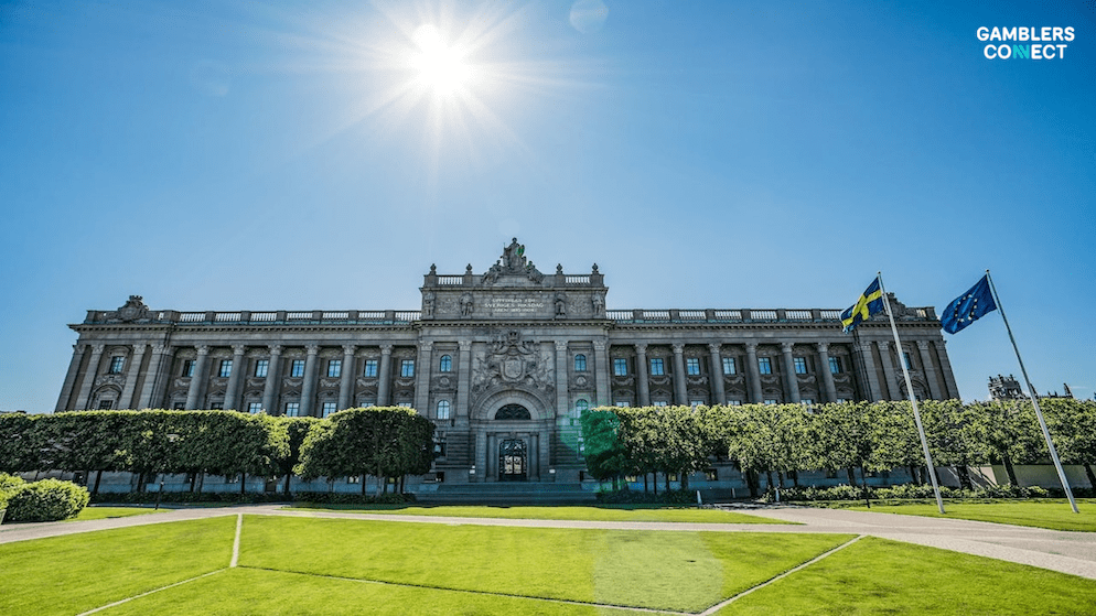 A wide shot of the Swedish Riksdag building with the Swedish and EU flags flying, symbolizing the legal framework governing sports integrity and gambling in Sweden.