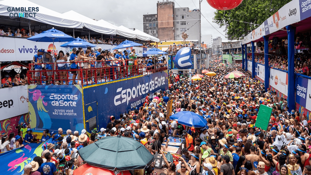 Massive crowds celebrate at the Esportes da Sorte sponsored Carnival in Brazil, featuring vibrant blue and yellow branding on a parade float.